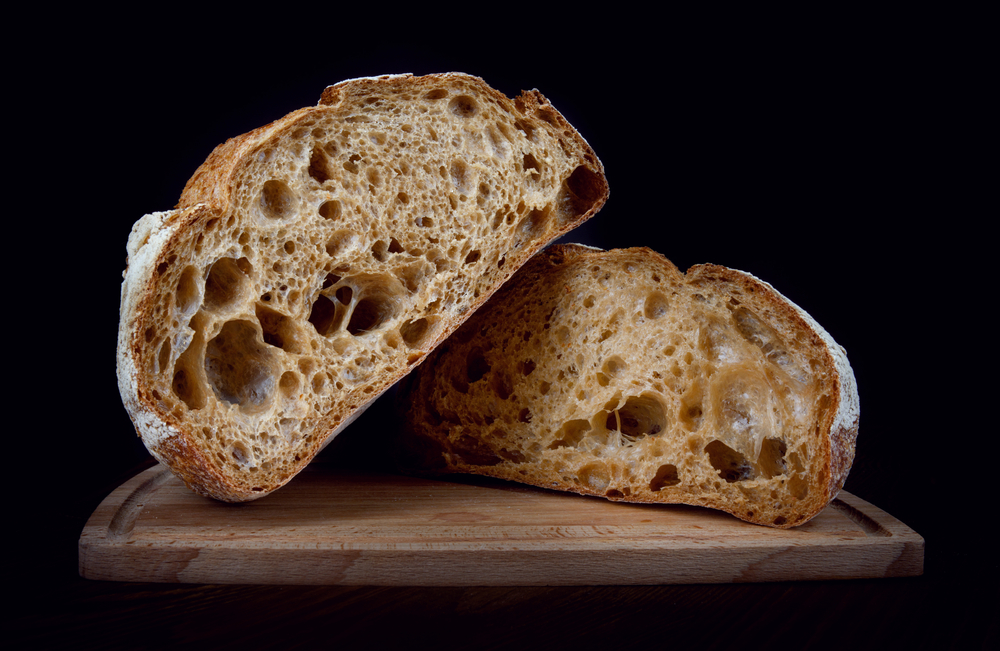 A loaf of rye bread cut in half on a wooden cutting board