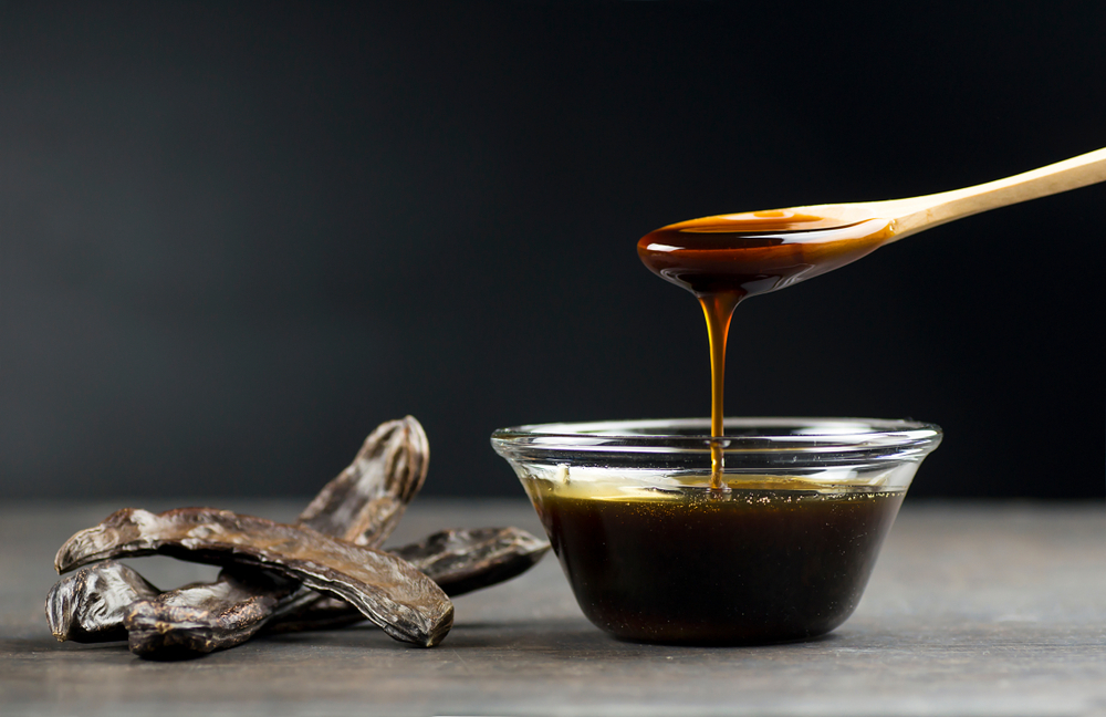 carob molasses in glass bowl and in wooden spoon