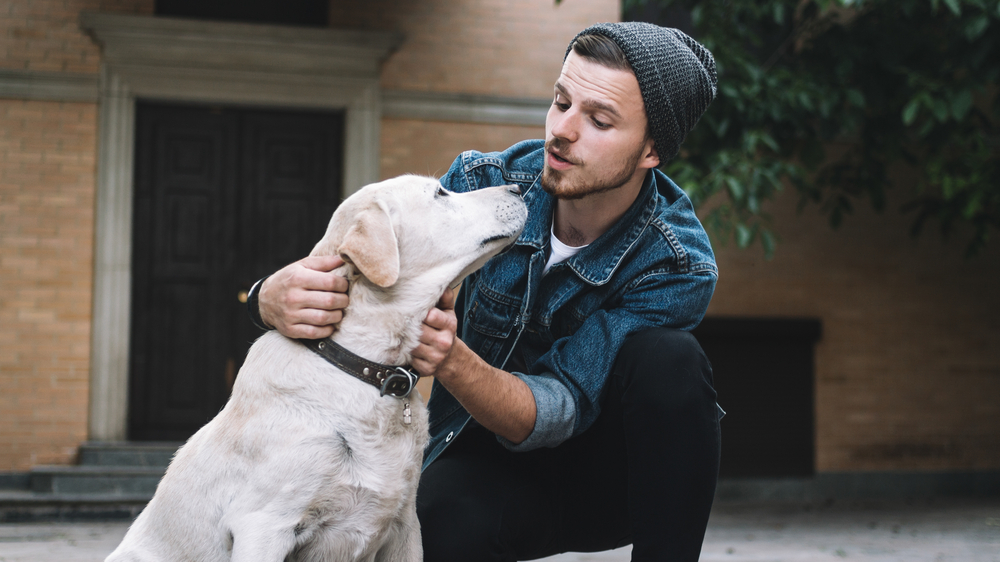 a guy squatting and talking to his dog outdoor