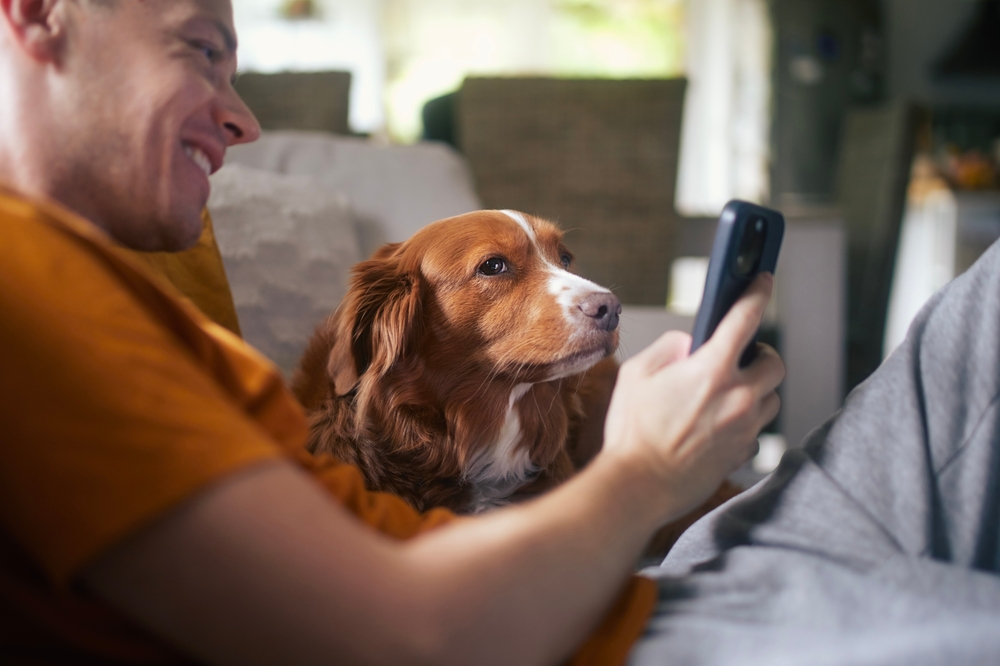 man using his phone with his dog on couch