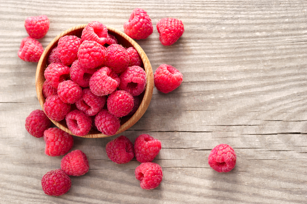 Ripe sweet raspberries in bowl on wooden table